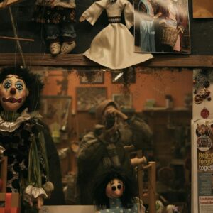 A vintage shop mirror reflects a quirky display of dolls and puppets.