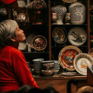 Elderly person with gray hair surrounded by traditional pottery in an artisan shop.